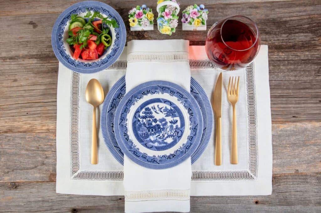 Empty food tableware, ceramic plate, spice little bowls, knife, fork with a old linen cloth on a old vintage wooden table.