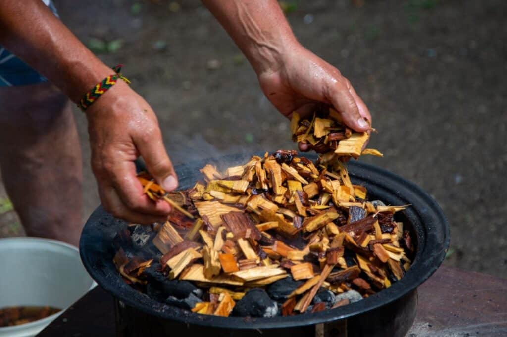 Adding soaked wood chips to the burning charcoal For Smoking Meat On Barbecue.