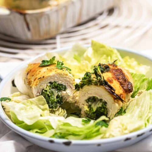 A close-up of two golden-brown chicken roll-ups stuffed with creamy spinach and herbs, served on a bed of fresh green lettuce in a light blue dish.