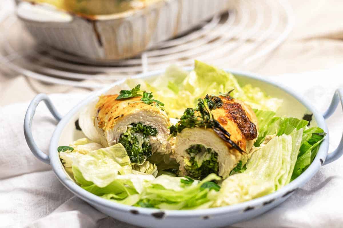 A close-up of two golden-brown chicken roll-ups stuffed with creamy spinach and herbs, served on a bed of fresh green lettuce in a light blue dish.