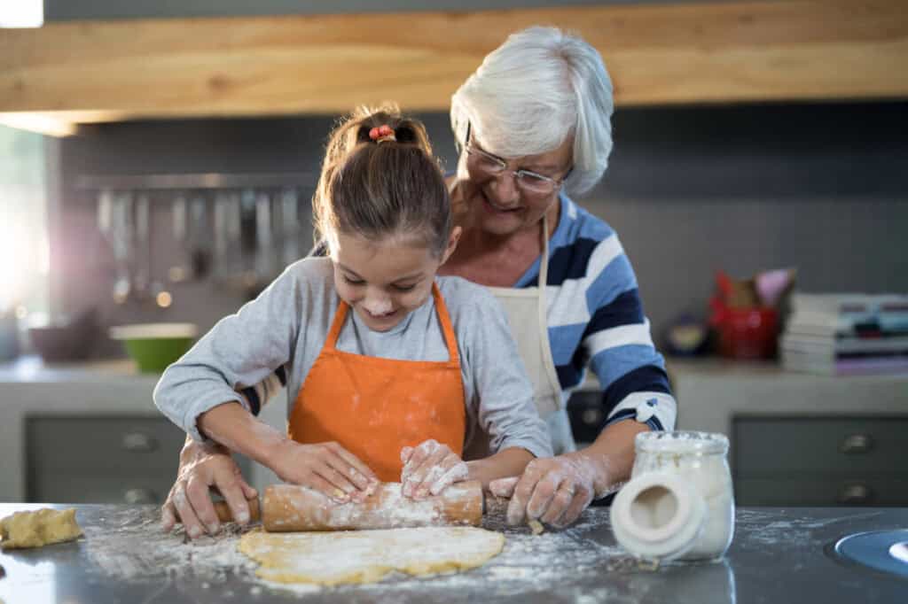 Grandmother helping granddaughter to flatten dough.