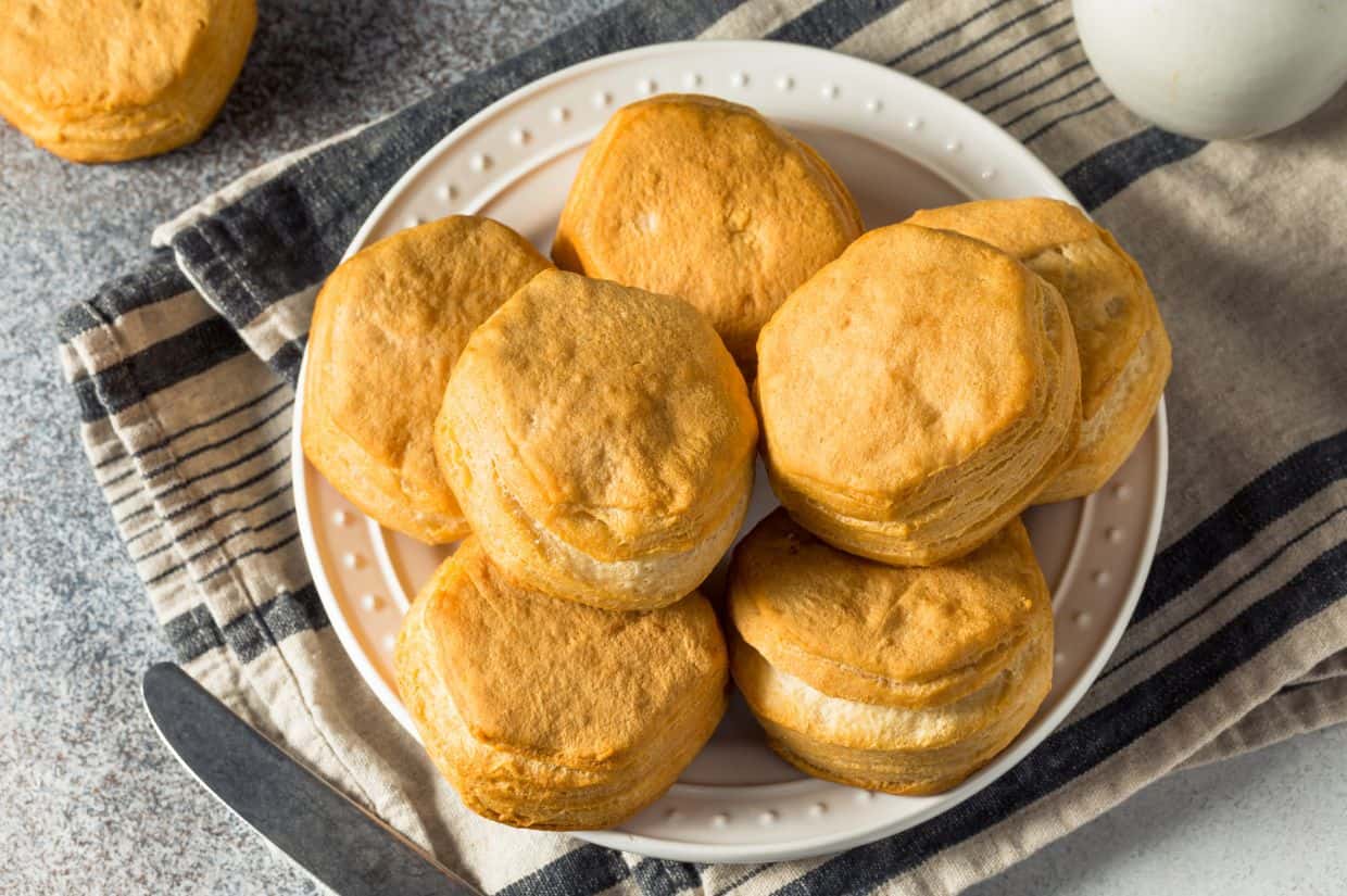 Three golden-brown biscuits are stacked, with the top one missing a bite. A small sprig of greenery with red berries is visible in the corner.