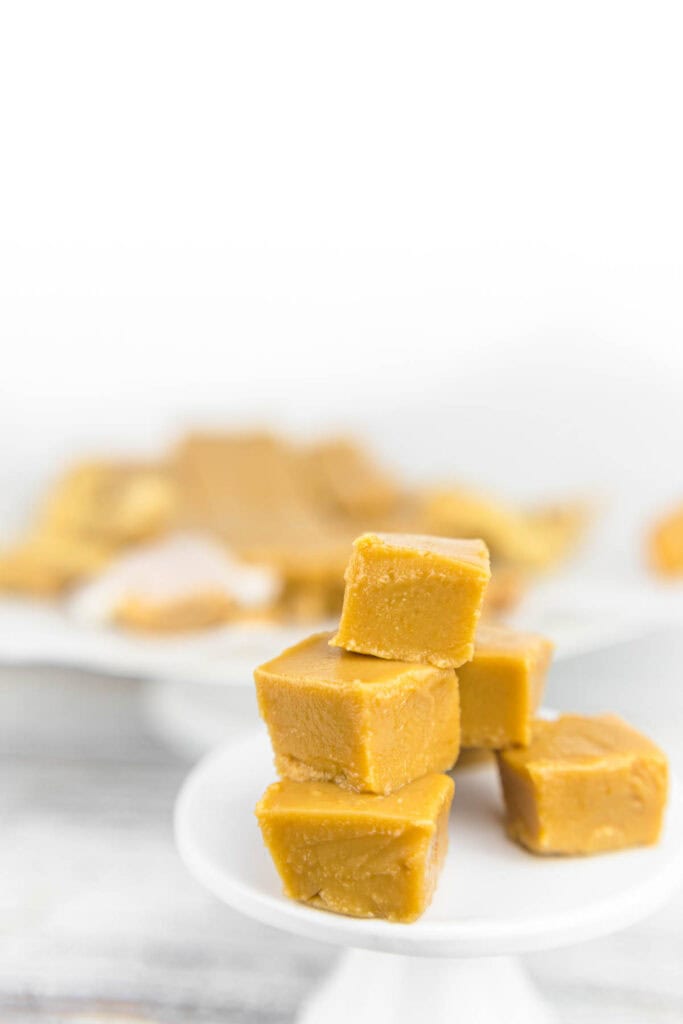 A close-up of creamy, smooth peanut butter fudge squares stacked neatly on a plate.