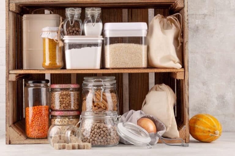 A neatly organized pantry shelf featuring glass jars filled with various dry goods, including lentils, pasta, and spices, alongside storage containers for flour and rice.