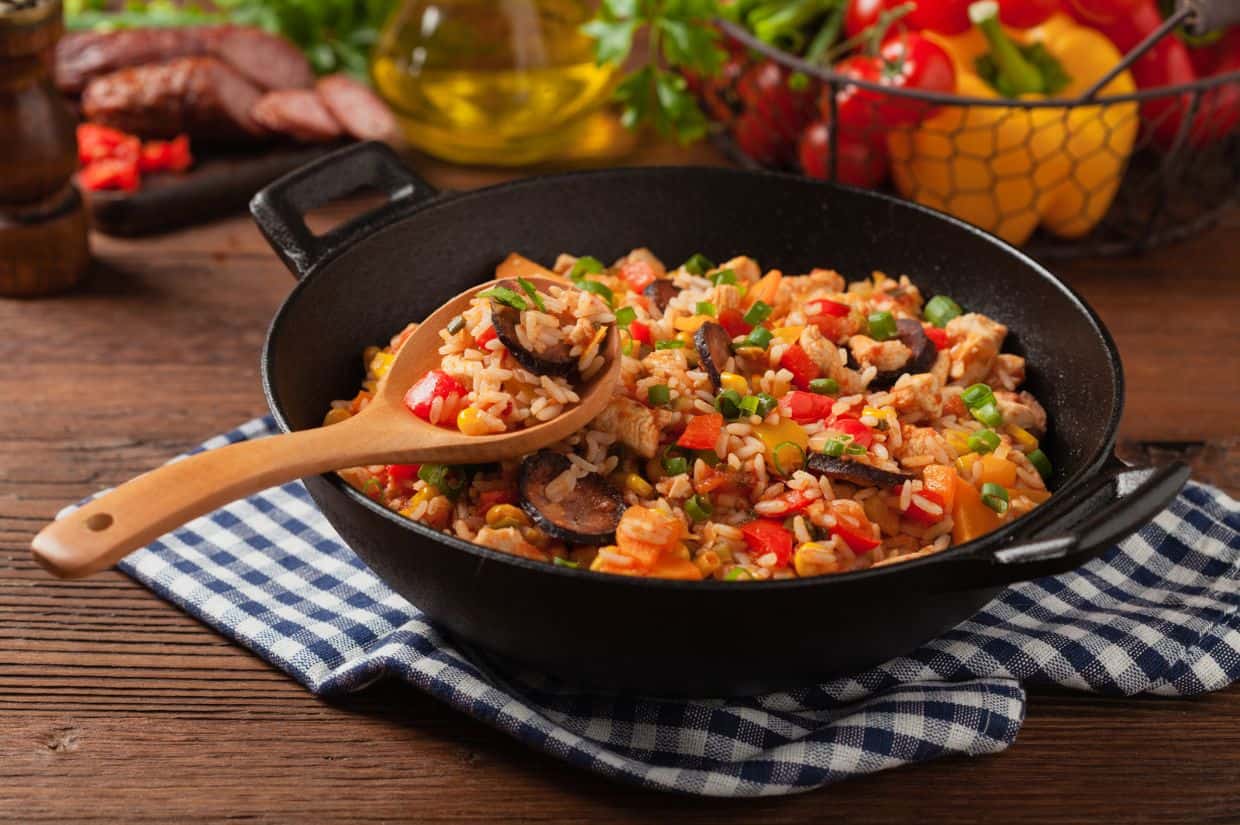 A black bowl filled with jambalaya, featuring shrimp, sausage, rice, and vegetables in a reddish sauce, garnished with chopped herbs.