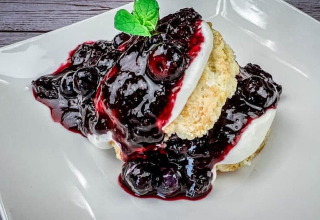 A blueberry shortcake topped with whipped cream and fresh blueberries, garnished with a mint leaf.
