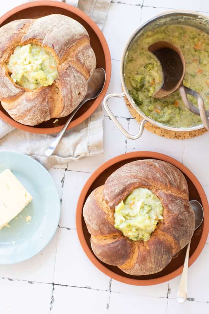 Two sourdough bread bowls filled with broccoli cheddar soup.