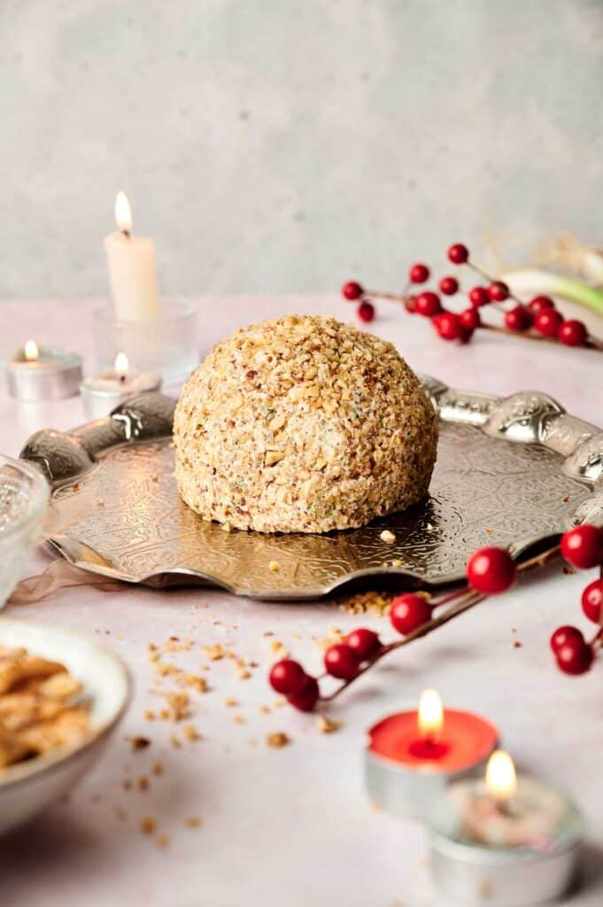 Holiday cheese ball coated in nuts, surrounded by red berries and candles.