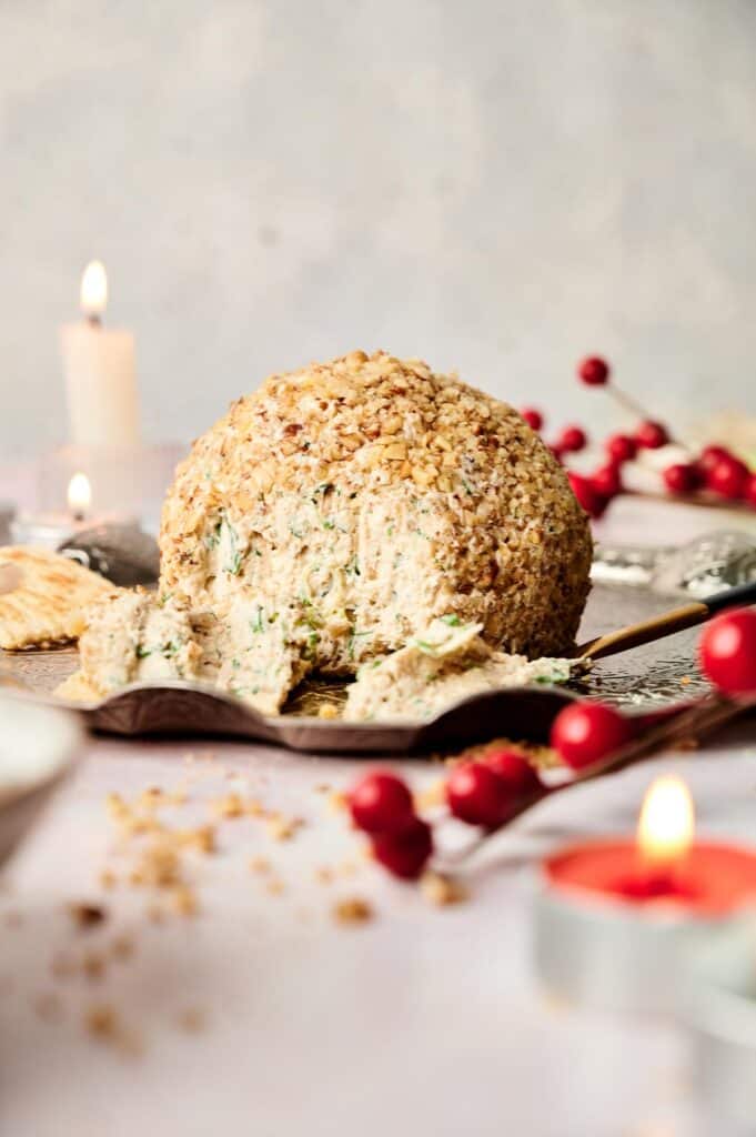 Nut-covered cheese ball with holiday decorations and candles.