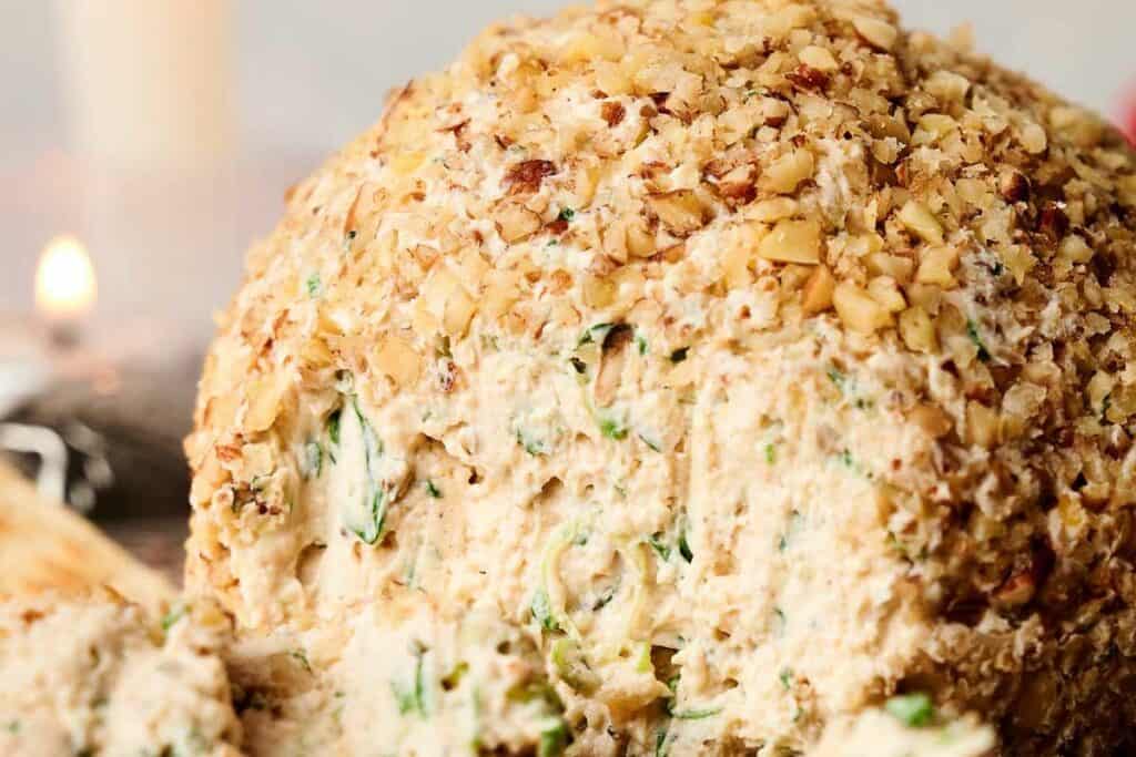 Close-up of a cheese ball coated in chopped nuts, with a creamy cheese and herb filling.