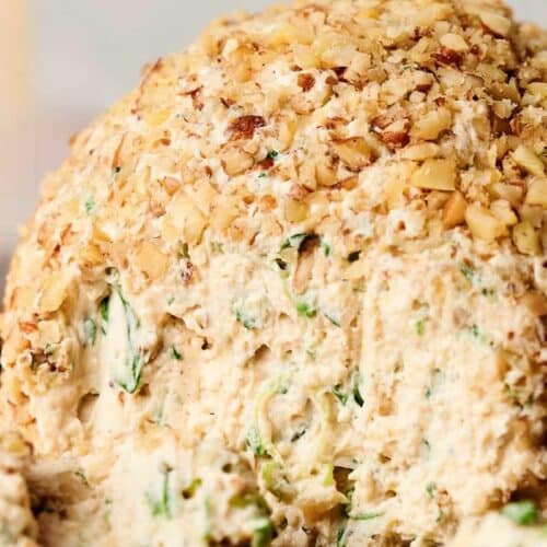 Close-up of a cheese ball coated in chopped nuts, with a creamy cheese and herb filling.