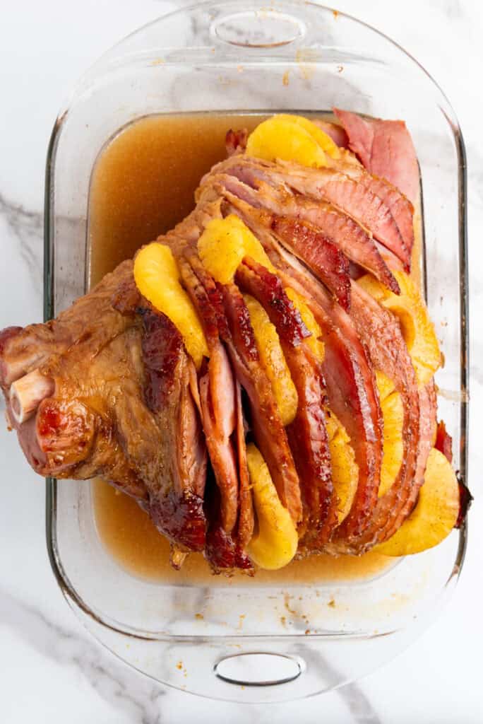 Slices of juicy, caramelized ham with visible pineapple rings in a glass baking dish.