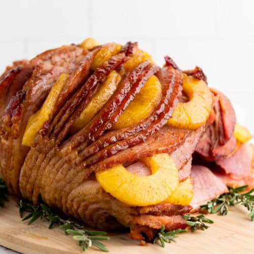 A ham covered in a shiny brown sugar glaze surrounded by pineapple slices.