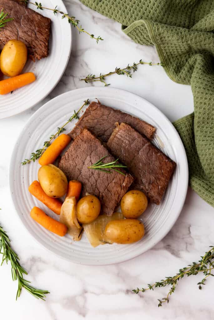 Tender, slow-cooked rump roast served with a side of vegetables, garnished with fresh herbs.