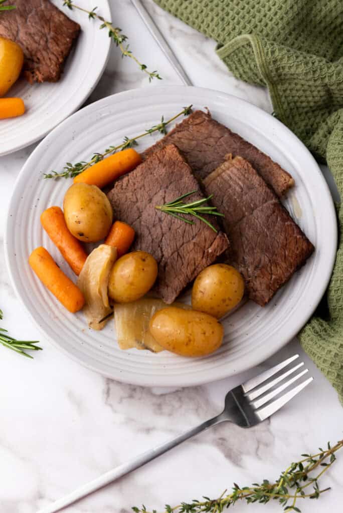 Slow-cooked rump roast served on a plate with a side of potatoes and carrots.