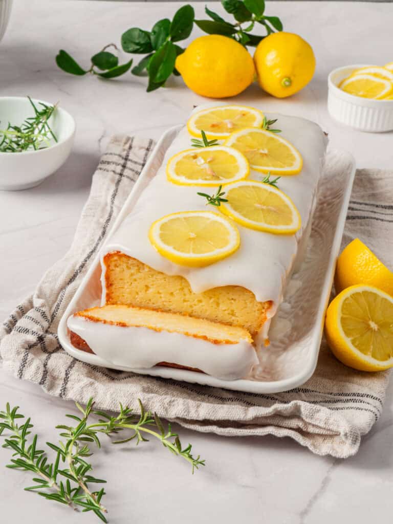 A golden lemon loaf cake with a shiny, sweet glaze, accompanied by a few sprigs of fresh mint.