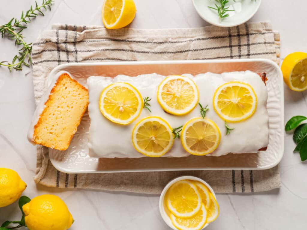 A freshly baked lemon loaf cake serve on a plate, garnished with lemon slices.