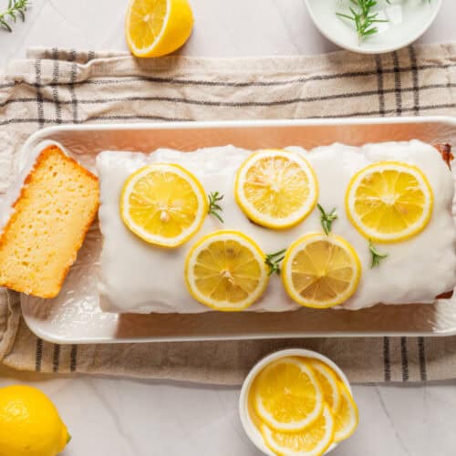 A freshly baked lemon loaf cake serve on a plate, garnished with lemon slices.