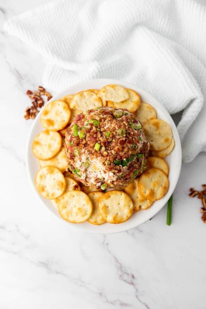 A holiday cheeseball featuring bacon, pecans, and green onion, ready to be enjoyed with crackers.