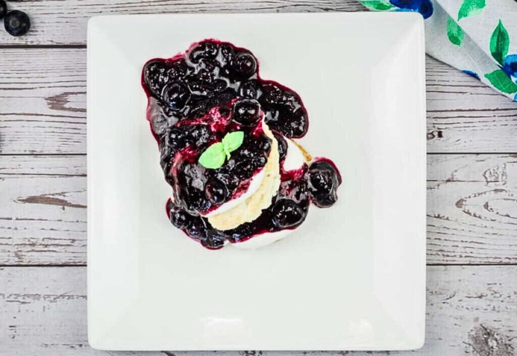Image of a serving of blueberry shortcake with cream and fresh blueberries on top.