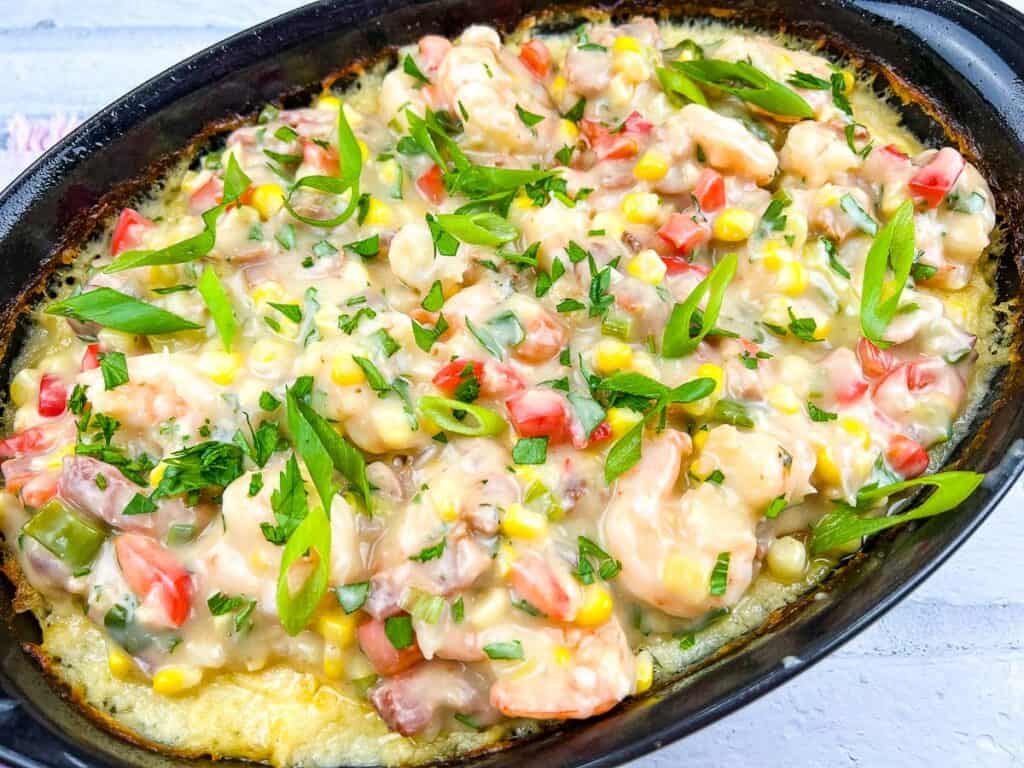 Close-up of shrimp and grits casserole with colorful veggies and spices.