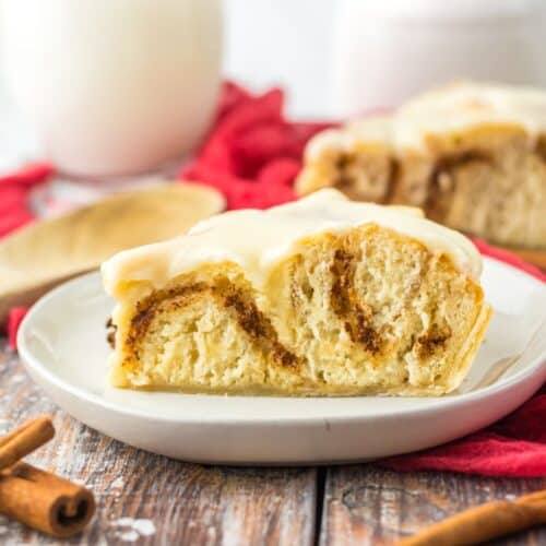 Cinnamon roll pie served on a white plate with cinnamon sticks nearby.