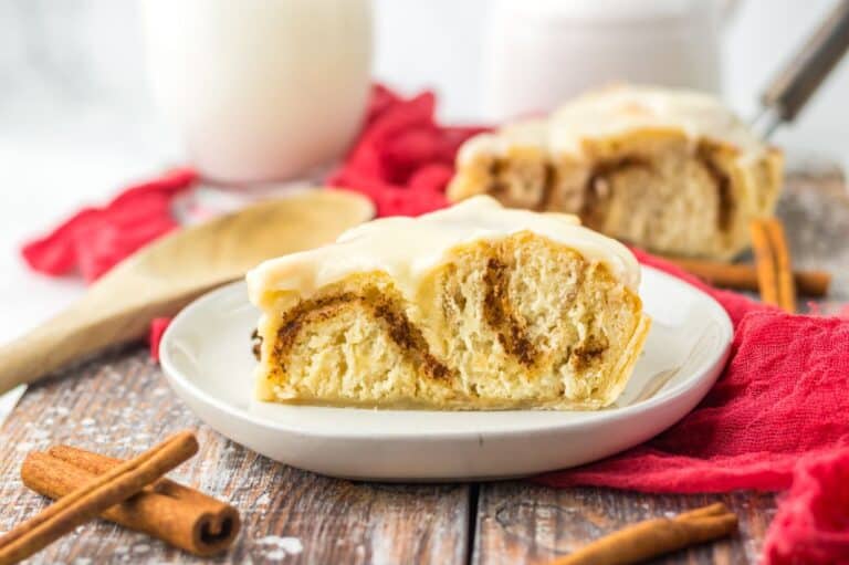 Cinnamon roll pie served on a white plate with cinnamon sticks nearby.