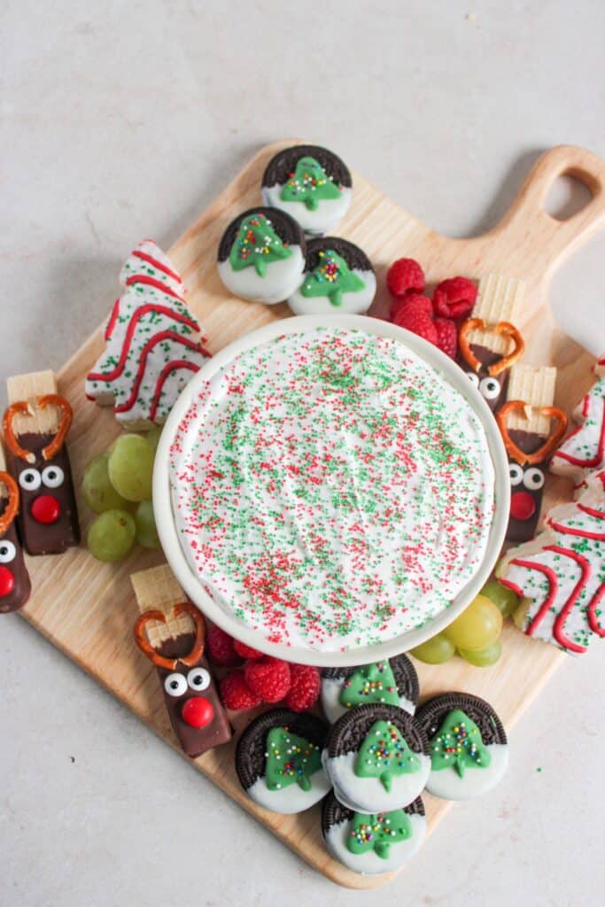 Holiday charcuterie board with colorful sprinkles, fresh strawberries, grapes, raspberries, and Christmas-themed desserts.