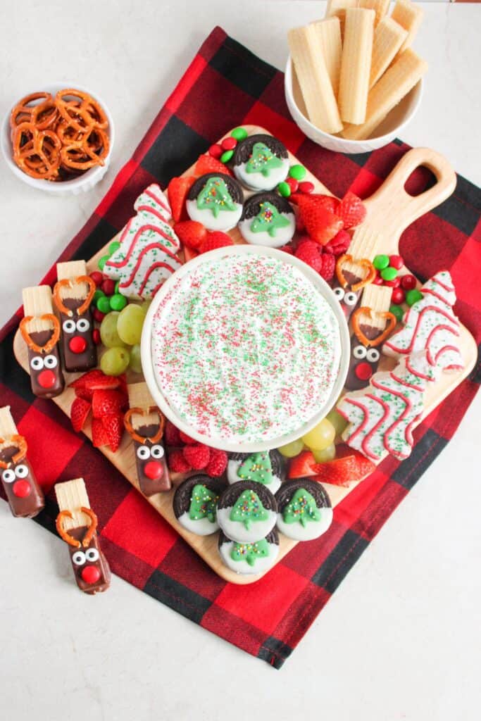 Christmas charcuterie board with reindeer-shaped treats, decorated cookies, and a fruit dip centerpiece.