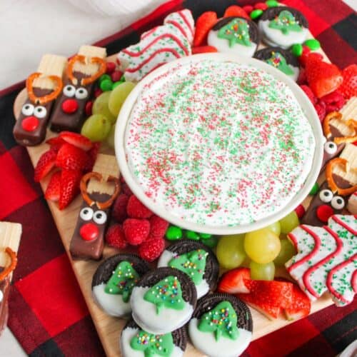 A festive Christmas charcuterie board with a bowl of sprinkled fruit dip surrounded by holiday-themed treats and fruits.