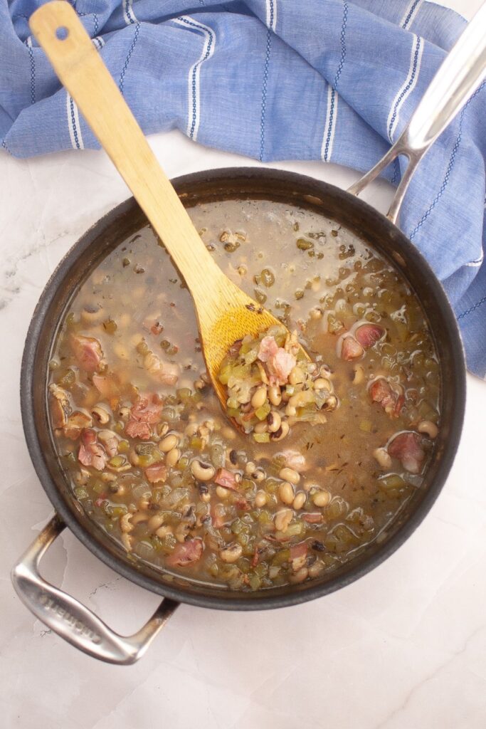 Black-eyed peas, diced ham, and green vegetables simmering in a pot.