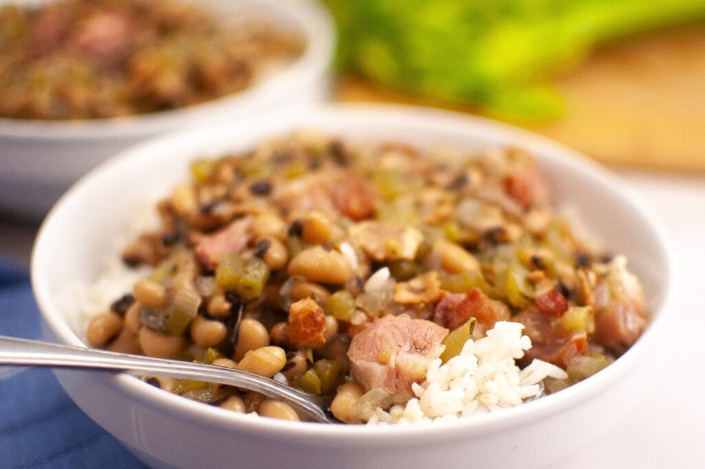 
A bowl of Hoppin' John, featuring black-eyed peas, rice, and diced ham, garnished with chopped green onions.