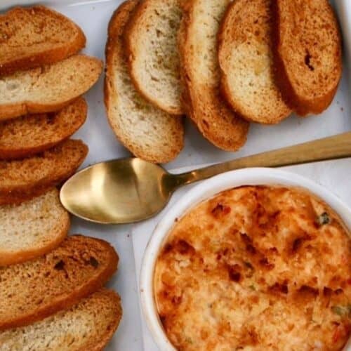 A bowl of hot crab and pimento cheese dip with a golden, bubbly surface is placed on a tray.