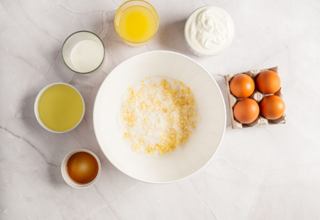 A bowl of lemon zest-sugar mixture surrounded with the rest of the wet ingredients.