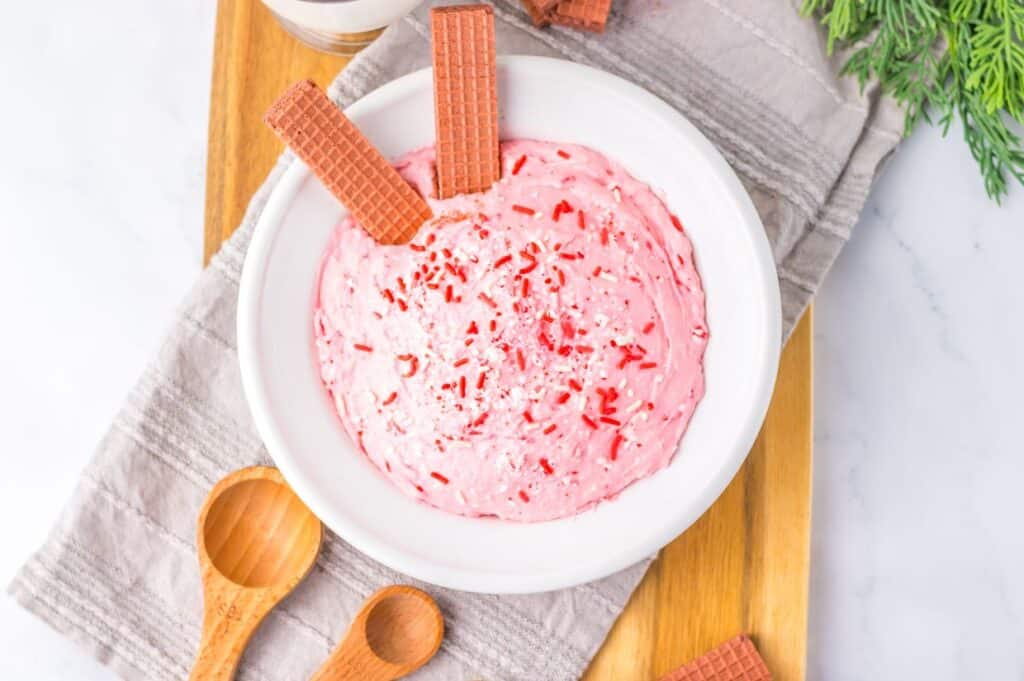 Bowl of peppermint fluff topped with red sprinkles and wafer cookies.