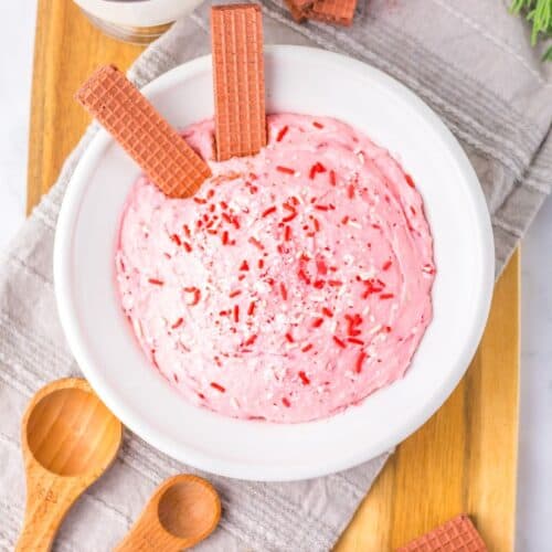 Bowl of peppermint fluff topped with red sprinkles and wafer cookies.