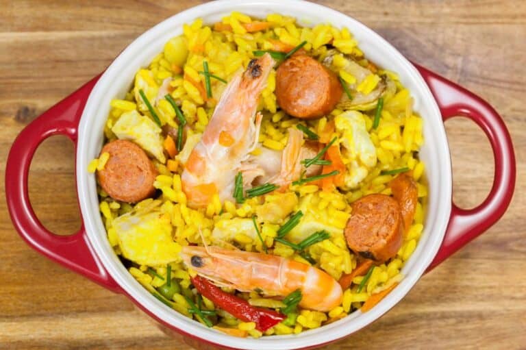 Spicy Cajun Jambalaya with sausage, shrimp and chicken in a red and white bowl on a wooden board.