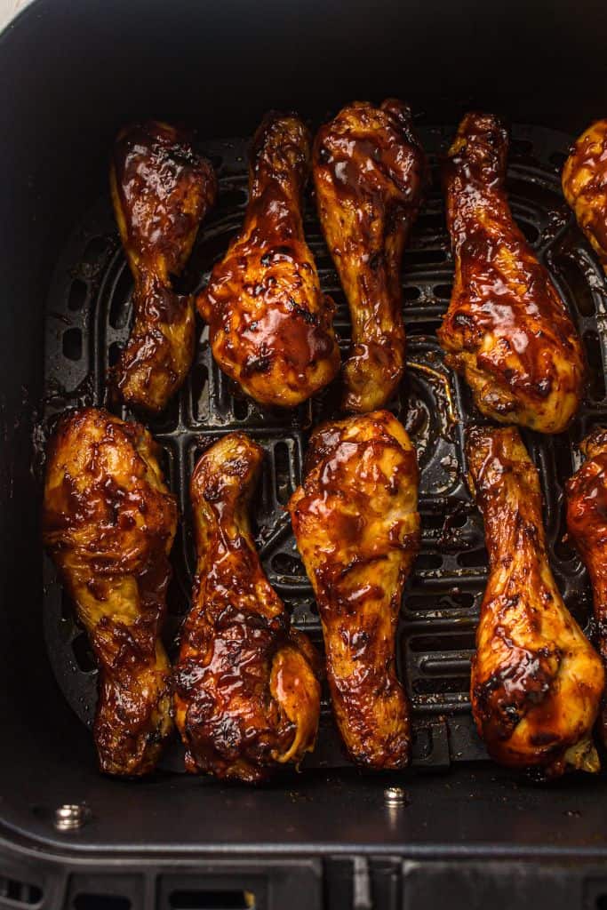 Cooked BBQ chicken drumsticks coated in a glossy barbecue sauce are arranged in an air fryer basket, showcasing a caramelized, flavorful glaze.