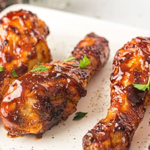 A close-up of crispy, air-fried BBQ chicken drumsticks glazed with a rich, glossy sauce and garnished with fresh parsley on a white plate.