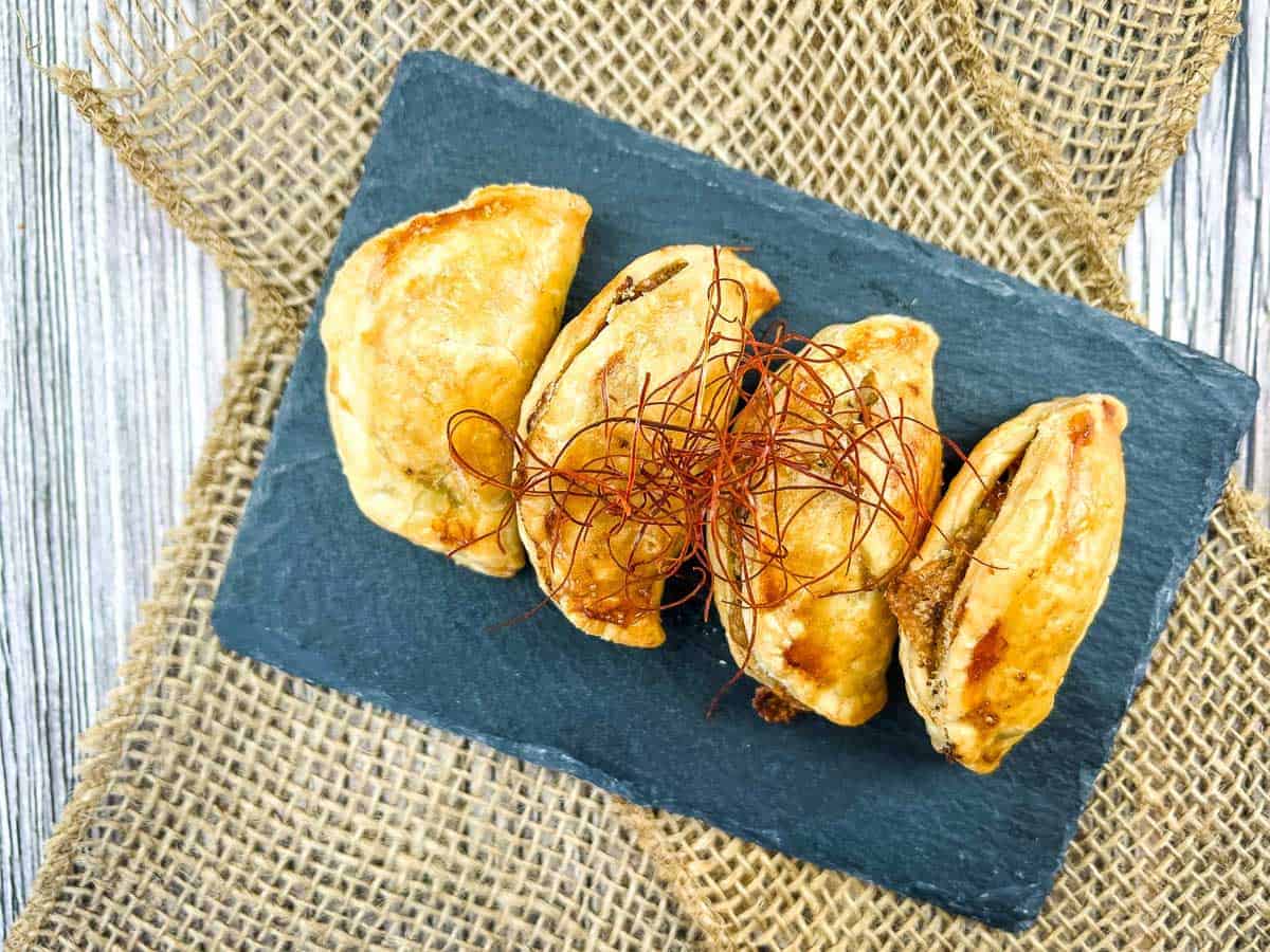 Four pieces of Air Fryer Beef Empanadas on a black rectangular slate.