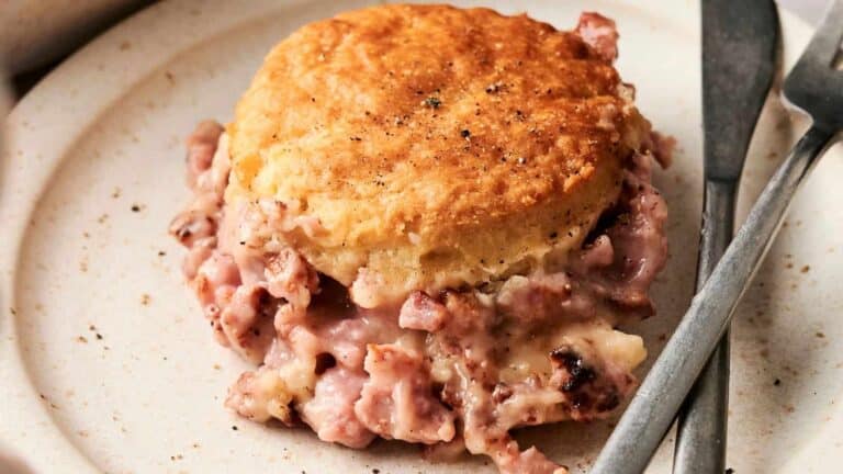 A plate with a biscuit topped with creamy sausage gravy, accompanied by a fork and knife.