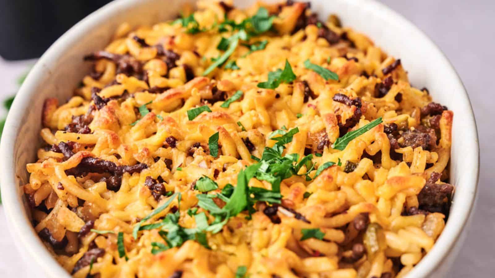 A baked dish with pasta, ground beef, melted cheese, and topped with fresh parsley.