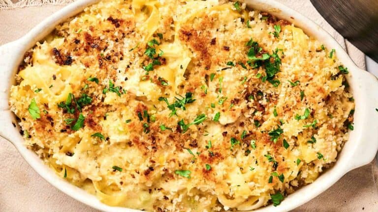 Baked pasta in a white dish, topped with golden breadcrumbs and garnished with parsley.