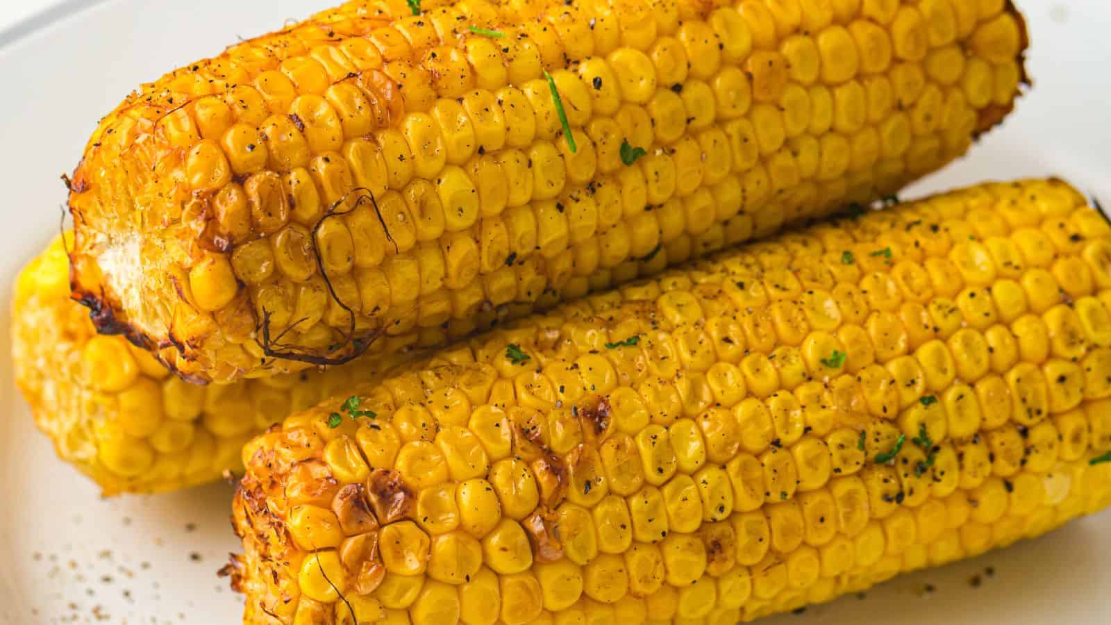 A close-up image of three seasoned and grilled ears of corn arranged on a plate.