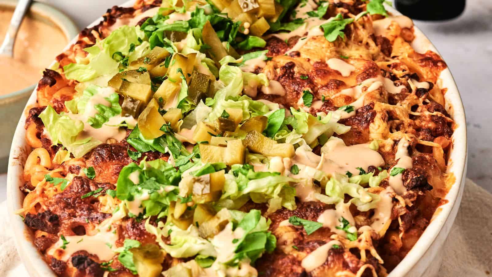 An air fryer hamburger casserole emerges from the kitchen, a baked dish topped with melted cheese, lettuce, pickles, and sauce in a round baking dish gracing the table.