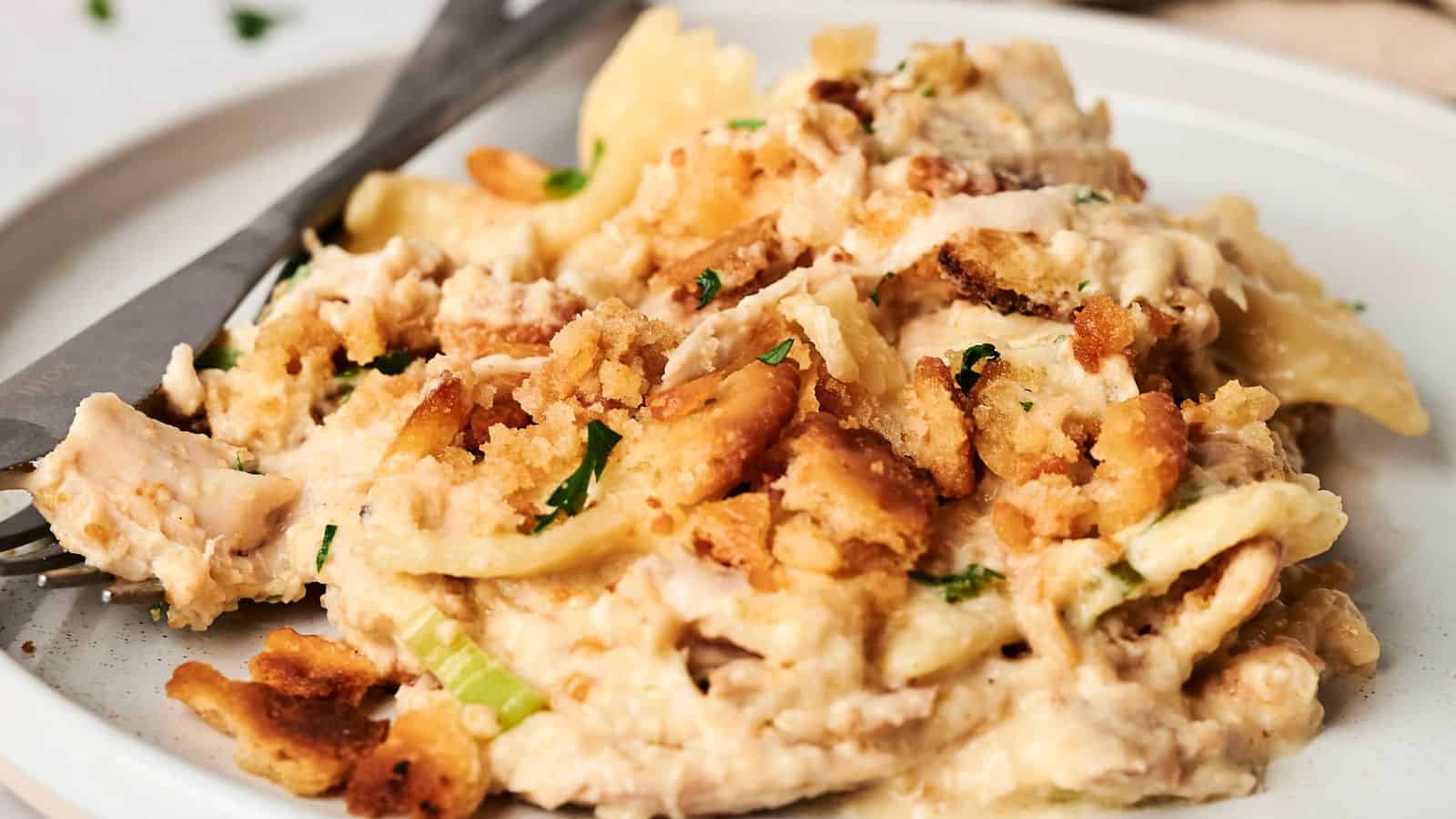 A plate of creamy chicken casserole topped with breadcrumbs and parsley, with a fork beside it.