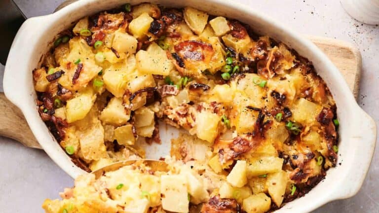 A baked casserole dish filled with cheesy potatoes and crispy bacon, garnished with chopped green onions, with a portion missing from the dish.