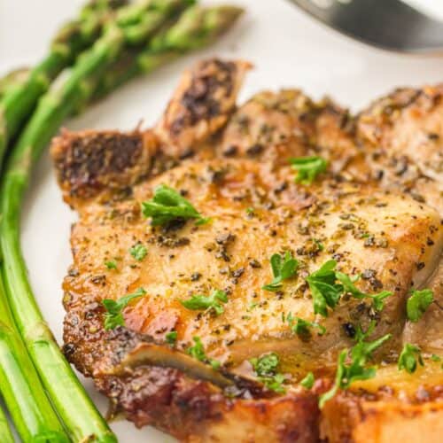 A close-up image of a golden-brown, seasoned pork chop garnished with fresh parsley on a white plate.