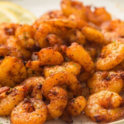 Seasoned and crispy air-fried shrimp served on a plate, garnished with fresh herbs and accompanied by lemon slices.