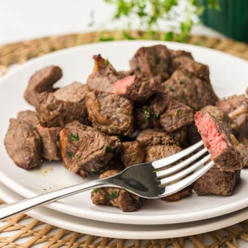 A plate of juicy, seasoned steak bites cooked in an air fryer, garnished with chopped herbs.